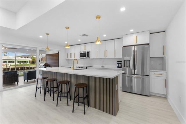 kitchen with a center island with sink, stainless steel appliances, hanging light fixtures, and white cabinets