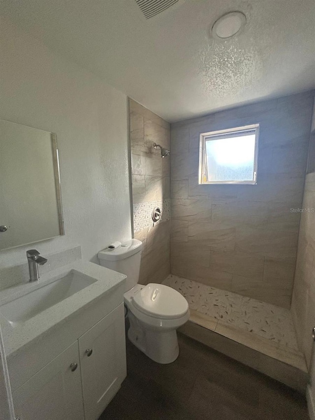 bathroom featuring vanity, a textured ceiling, toilet, and tiled shower