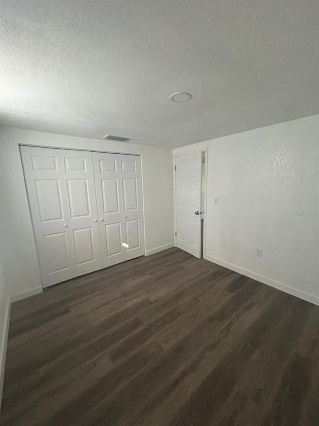 unfurnished bedroom with dark wood-type flooring, a textured ceiling, and a closet