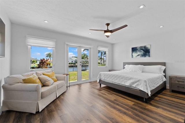 bedroom featuring dark hardwood / wood-style flooring, access to exterior, ceiling fan, a water view, and a textured ceiling