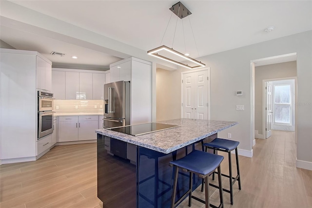 kitchen featuring white cabinets, light wood finished floors, stainless steel appliances, and backsplash