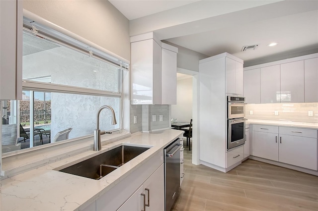 kitchen featuring visible vents, white cabinets, appliances with stainless steel finishes, light stone counters, and a sink