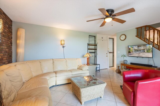 tiled living room featuring ceiling fan, a textured ceiling, and brick wall