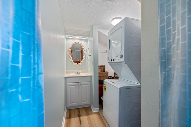 bathroom featuring stacked washer / dryer, wood-type flooring, vanity, and a textured ceiling