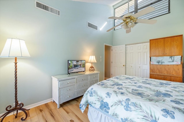 bedroom featuring ceiling fan, a towering ceiling, light wood-type flooring, and a closet