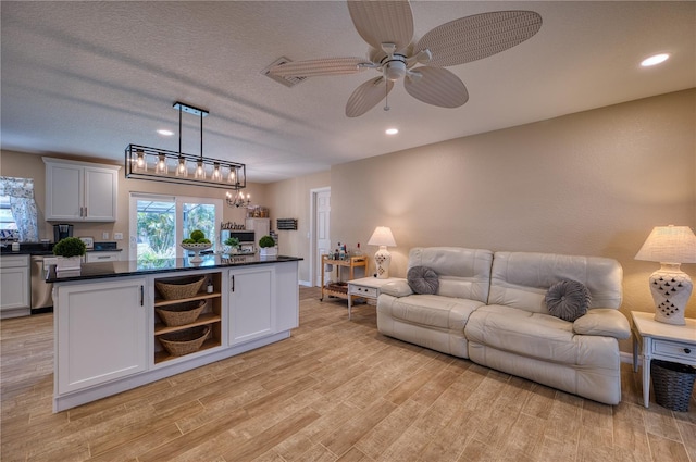 living room with ceiling fan, a textured ceiling, and light wood-type flooring