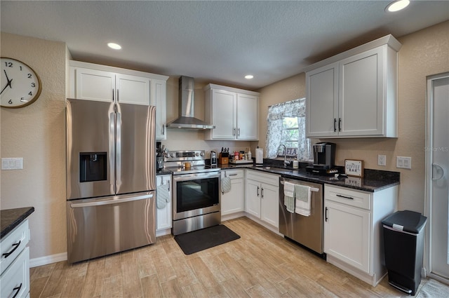 kitchen with white cabinets, stainless steel appliances, sink, and wall chimney exhaust hood