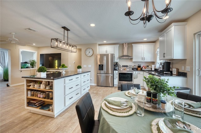 kitchen with wall chimney range hood, appliances with stainless steel finishes, white cabinetry, decorative light fixtures, and light wood-type flooring