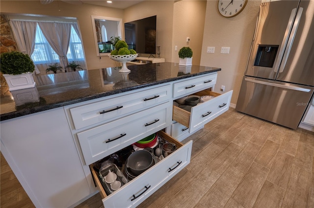 kitchen with stainless steel refrigerator with ice dispenser, white cabinetry, light hardwood / wood-style flooring, and dark stone countertops