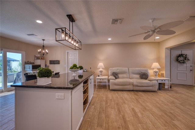 kitchen with pendant lighting, dark stone counters, a center island, a textured ceiling, and light hardwood / wood-style flooring