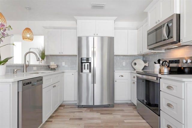 kitchen featuring sink, light hardwood / wood-style flooring, hanging light fixtures, appliances with stainless steel finishes, and white cabinets