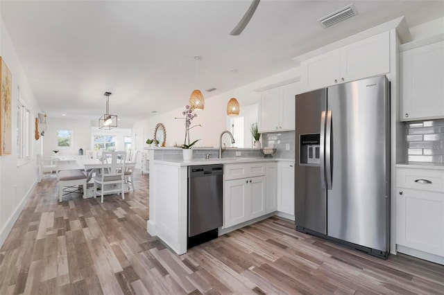 kitchen with visible vents, a sink, tasteful backsplash, stainless steel appliances, and a peninsula