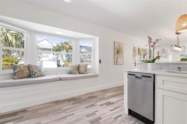 kitchen featuring white cabinetry, sink, hanging light fixtures, stainless steel dishwasher, and light hardwood / wood-style flooring