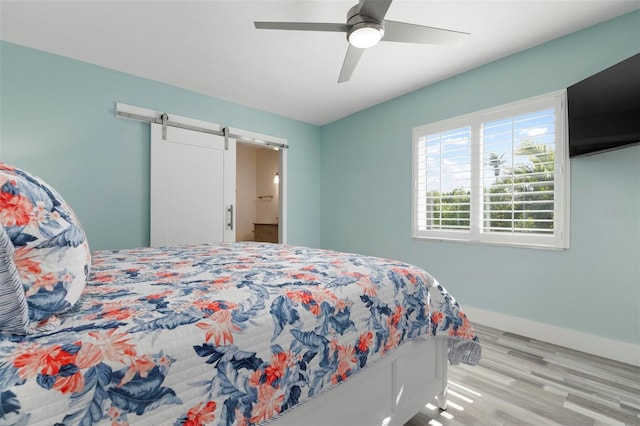 bedroom with connected bathroom, a barn door, ceiling fan, and light wood-type flooring