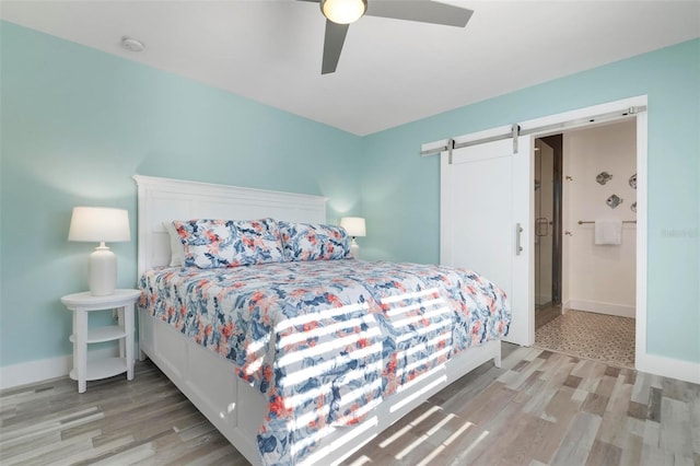 bedroom featuring hardwood / wood-style floors, a barn door, ceiling fan, and ensuite bathroom