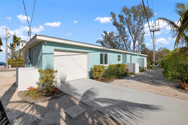 view of front facade with stucco siding, driveway, a garage, and fence