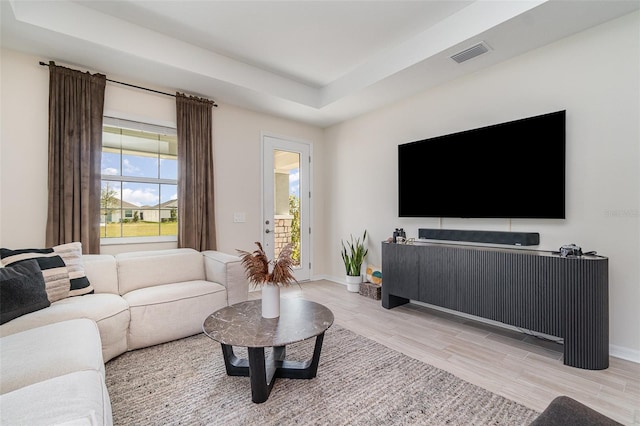 living area with visible vents, light wood-style flooring, a raised ceiling, and baseboards