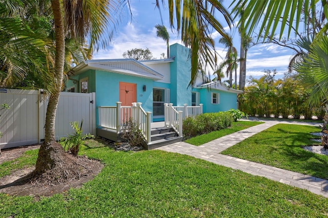 bungalow-style house with a gate, fence, a front lawn, and stucco siding