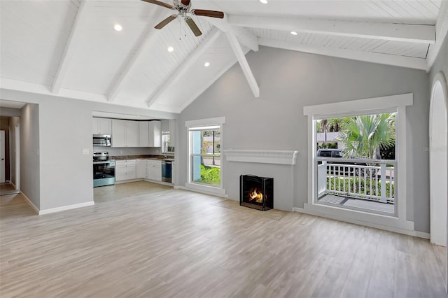 unfurnished living room with baseboards, a fireplace with flush hearth, beamed ceiling, light wood-type flooring, and high vaulted ceiling