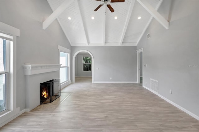 unfurnished living room featuring light wood-type flooring, a lit fireplace, visible vents, and beam ceiling