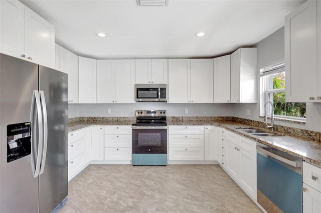 kitchen featuring appliances with stainless steel finishes, a sink, light stone counters, and white cabinets