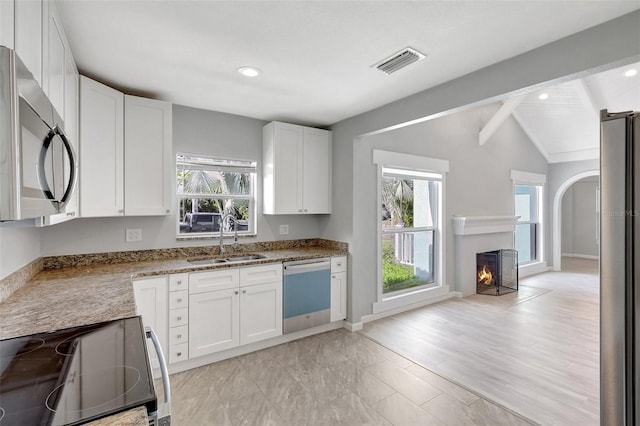 kitchen featuring visible vents, lofted ceiling with beams, appliances with stainless steel finishes, white cabinets, and a sink