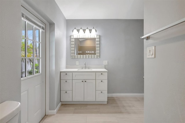 bathroom with toilet, wood finished floors, vanity, and baseboards