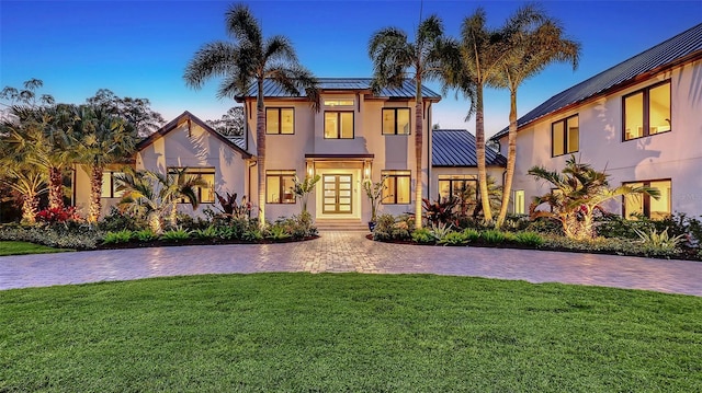 view of front of property with a standing seam roof, metal roof, a lawn, and stucco siding