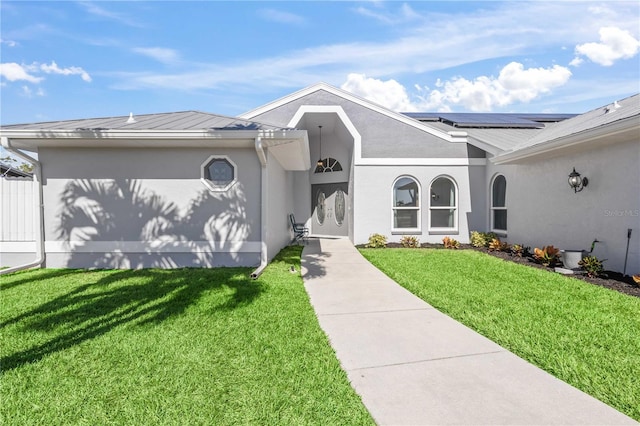 view of front of house featuring stucco siding, roof mounted solar panels, metal roof, and a front yard