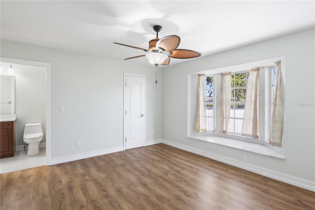 unfurnished bedroom featuring baseboards, a ceiling fan, wood finished floors, and ensuite bathroom