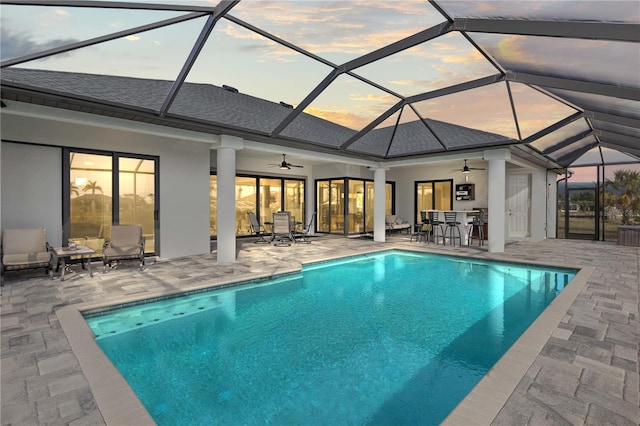 pool at dusk with ceiling fan, a lanai, an outdoor bar, and a patio area