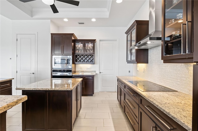 kitchen featuring wall chimney range hood, stainless steel appliances, a raised ceiling, and a kitchen island