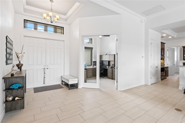 entryway with ornamental molding, an inviting chandelier, and a tray ceiling