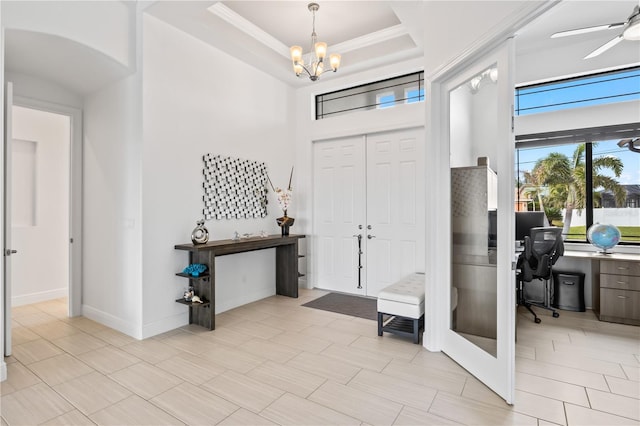 entryway featuring crown molding, a towering ceiling, ceiling fan with notable chandelier, and a tray ceiling