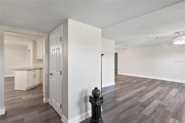 corridor with a textured ceiling, wood finished floors, visible vents, and baseboards