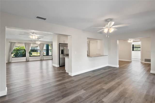 unfurnished living room featuring ceiling fan, dark wood-type flooring, visible vents, and baseboards