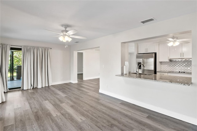 unfurnished living room with a ceiling fan, wood finished floors, visible vents, and baseboards