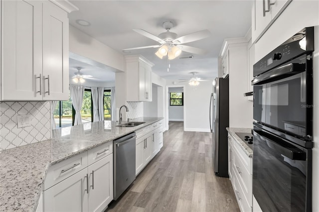 kitchen with white cabinets, light stone countertops, stainless steel appliances, and a sink