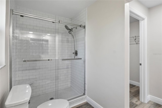 full bath with a stall shower, baseboards, toilet, wood finished floors, and a walk in closet