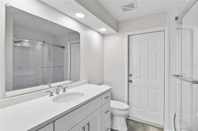 full bath featuring toilet, wood finished floors, vanity, visible vents, and a stall shower