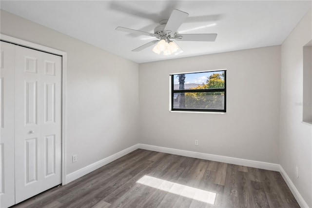 unfurnished bedroom with dark wood-style floors, a closet, a ceiling fan, and baseboards