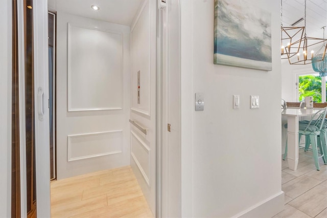 hall featuring elevator, a notable chandelier, and light wood-type flooring