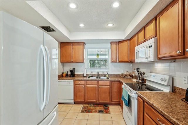 kitchen with sink, light tile patterned floors, a tray ceiling, white appliances, and backsplash