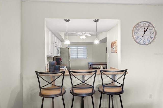 kitchen with white cabinetry, a kitchen bar, hanging light fixtures, and stainless steel refrigerator