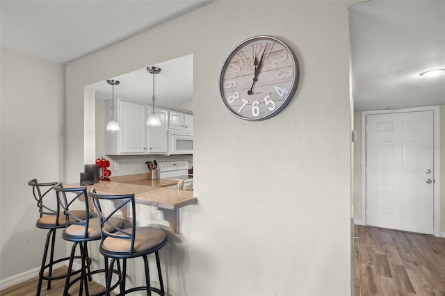 kitchen with white cabinetry, a breakfast bar, white appliances, and light wood-type flooring