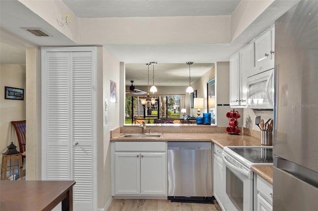 kitchen featuring sink, stainless steel appliances, white cabinets, decorative light fixtures, and light wood-type flooring