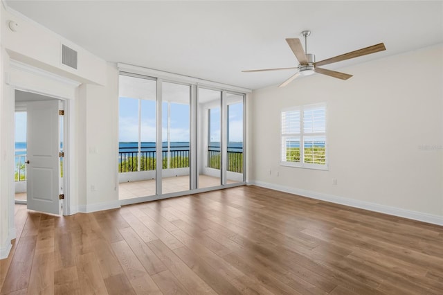 spare room with hardwood / wood-style floors, expansive windows, ceiling fan, and a water view