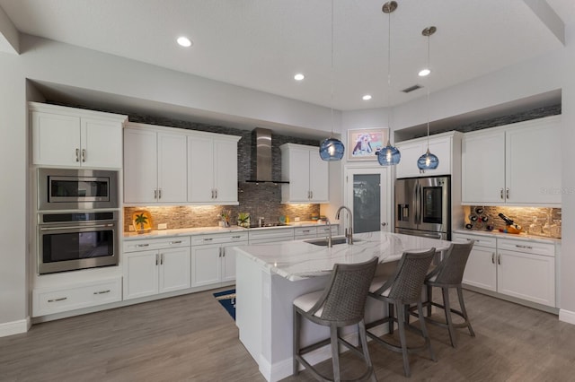 kitchen featuring wall chimney exhaust hood, appliances with stainless steel finishes, decorative light fixtures, and sink