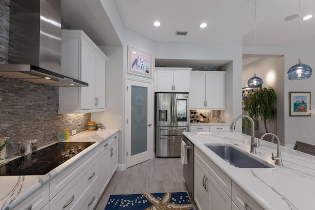 kitchen featuring appliances with stainless steel finishes, white cabinetry, sink, hanging light fixtures, and wall chimney exhaust hood