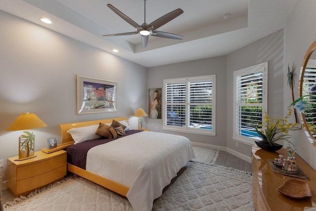 bedroom featuring a raised ceiling, ceiling fan, and light wood-type flooring